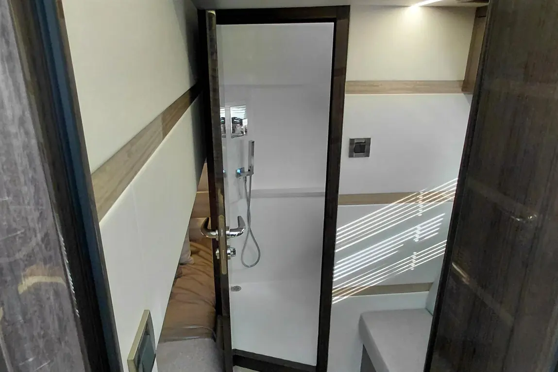 Modern bathroom with a glass shower door, showerhead, and grey decor; natural light reflects on the walls.